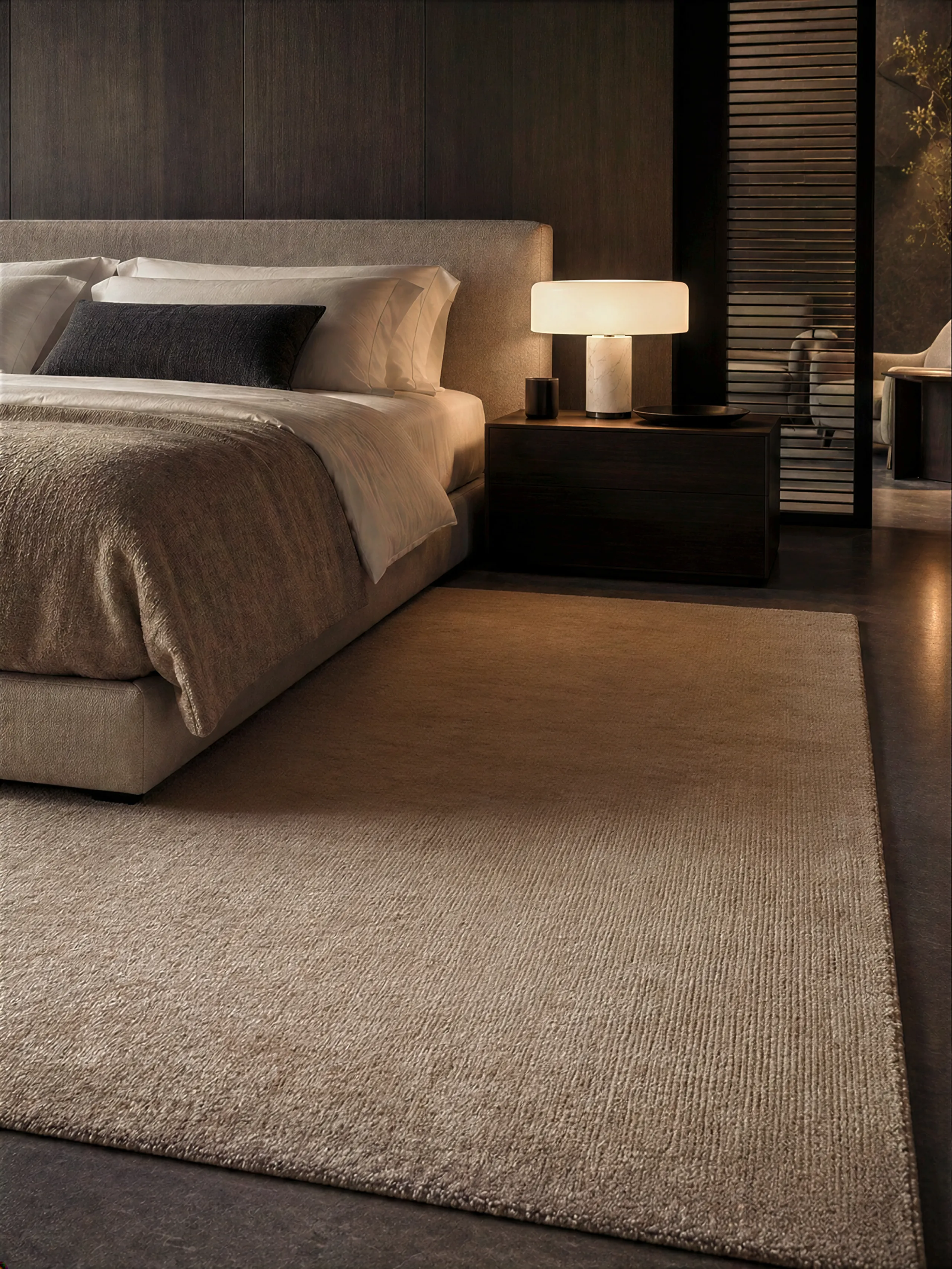 Luxe vloerkleed in warm taupe naast het bed in een chique hotelslaapkamer.