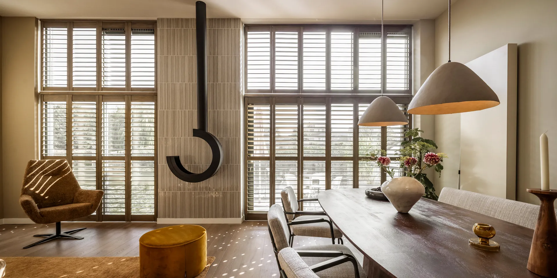 JASNO shutters op maat in Rustic Grey langs hoge ramen in een woonkamer met eettafel.